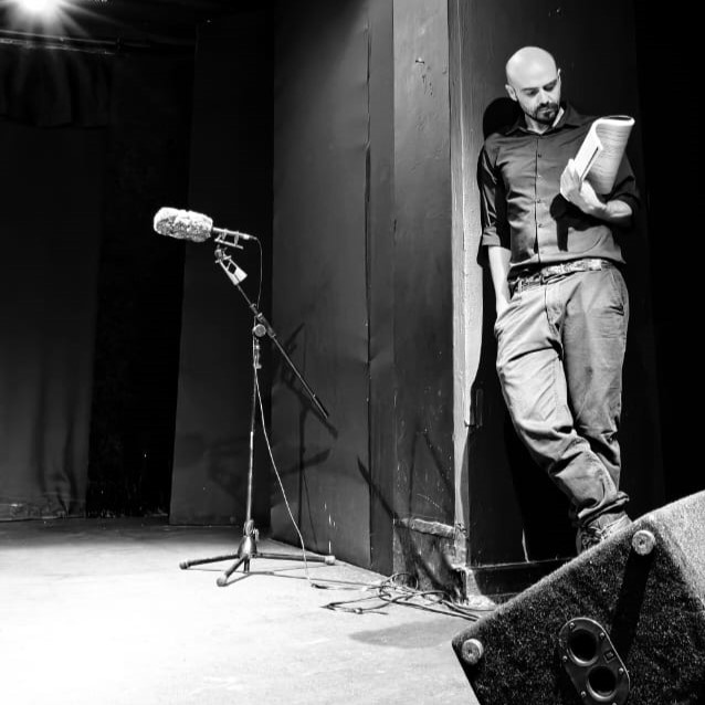 A dude looking at a script while standing beside a microphone.
